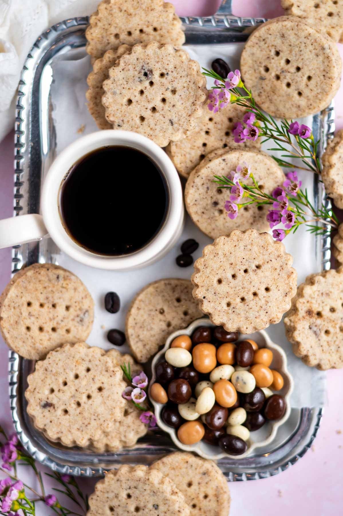 Espresso shortbread cookies stacked on a plate with coffee beans and a steaming cup of coffee in the background, warm light