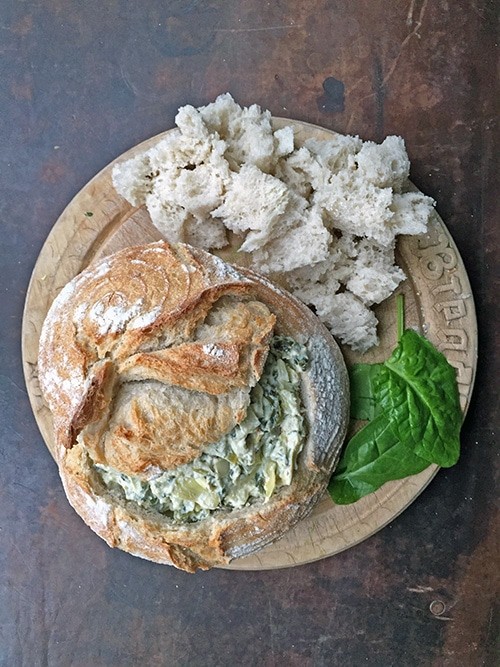 Close-up of bubbling, golden brown spinach artichoke dip in a rustic baking dish, with crusty bread for dipping