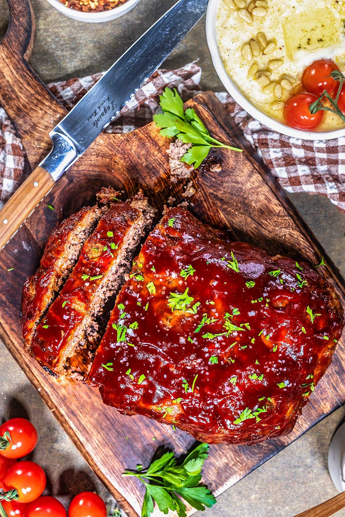 homemade meatloaf being sliced on a wooden cutting board, garnished with parsley