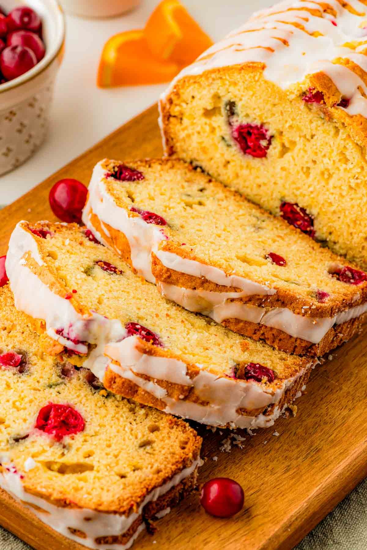 Close-up of a slice of cranberry orange bread with vanilla icing on a rustic wooden board, warm lighting