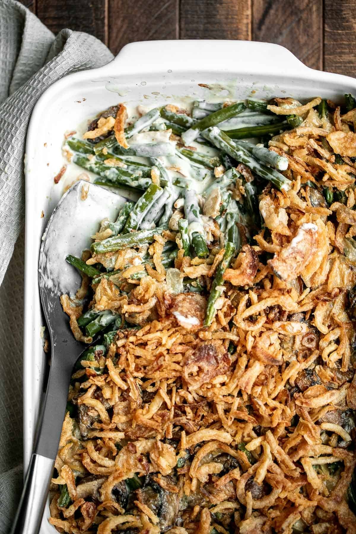 Gourmet green bean casserole with creamy pepper sauce, golden brown crispy onions on top, a sprig of fresh thyme