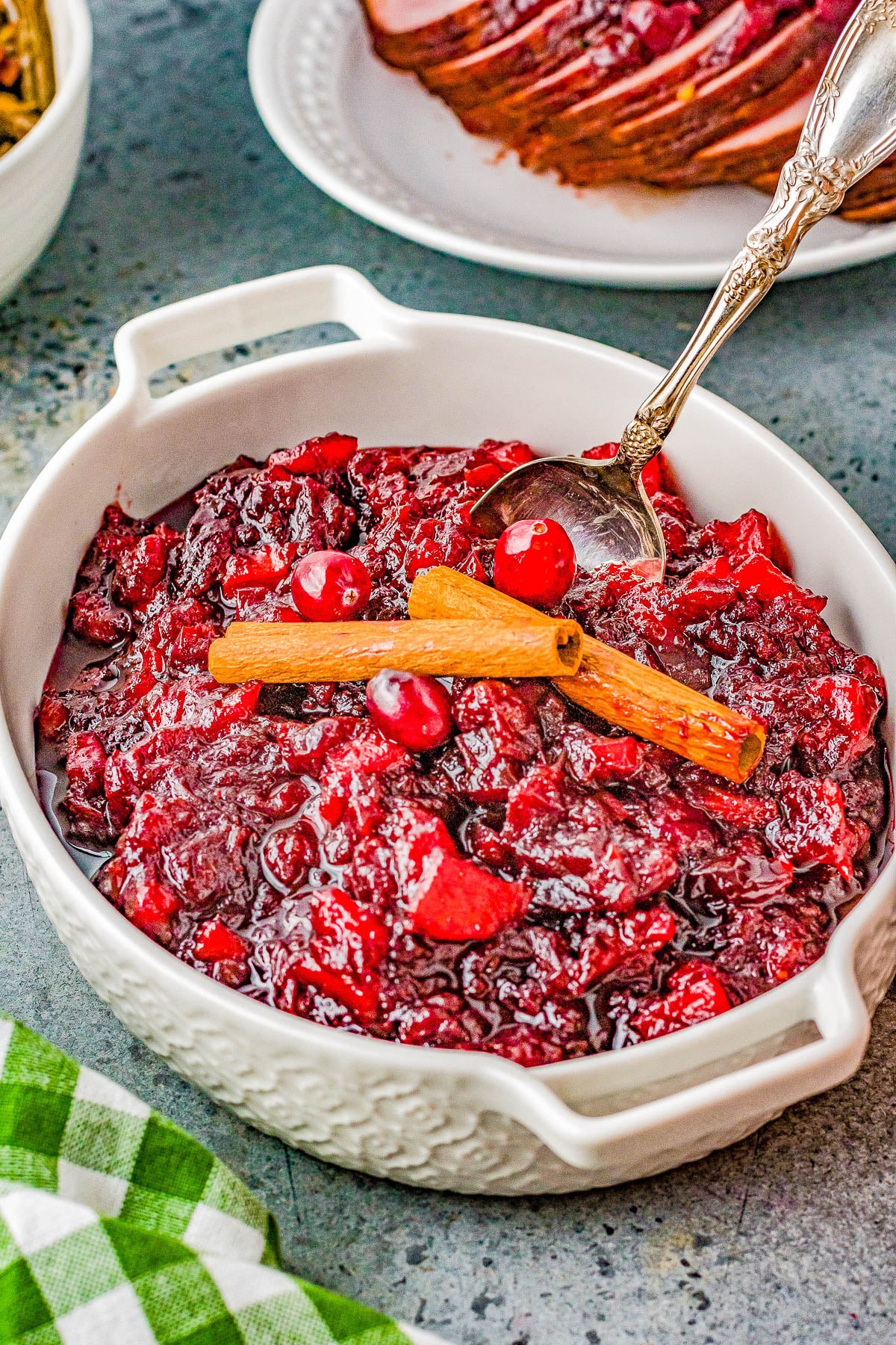 vibrant homemade cranberry apple sauce in a ceramic bowl with cinnamon sticks and fresh cranberries, cozy holiday setting