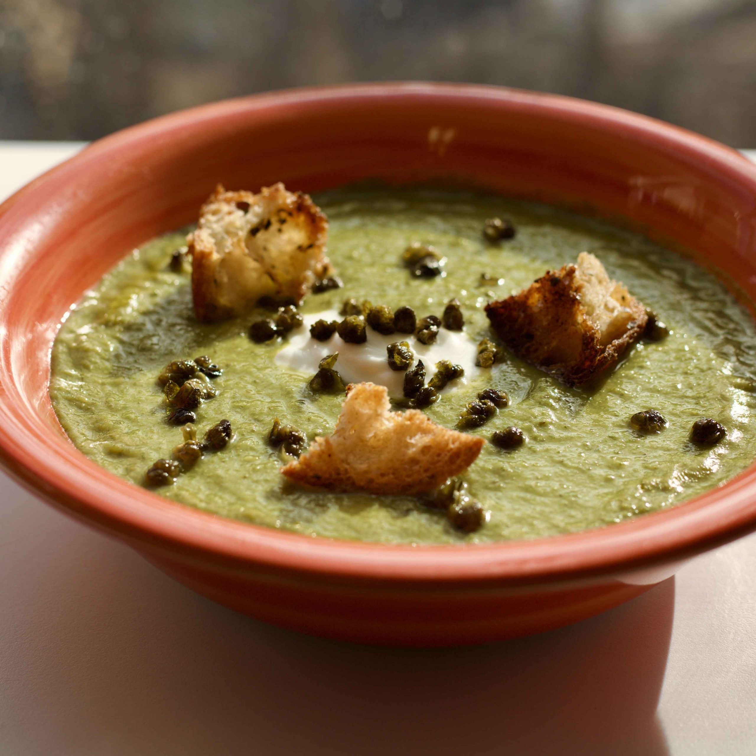 Rustic bowl of creamy green herb soup with fresh bread, cozy setting, comfort food style