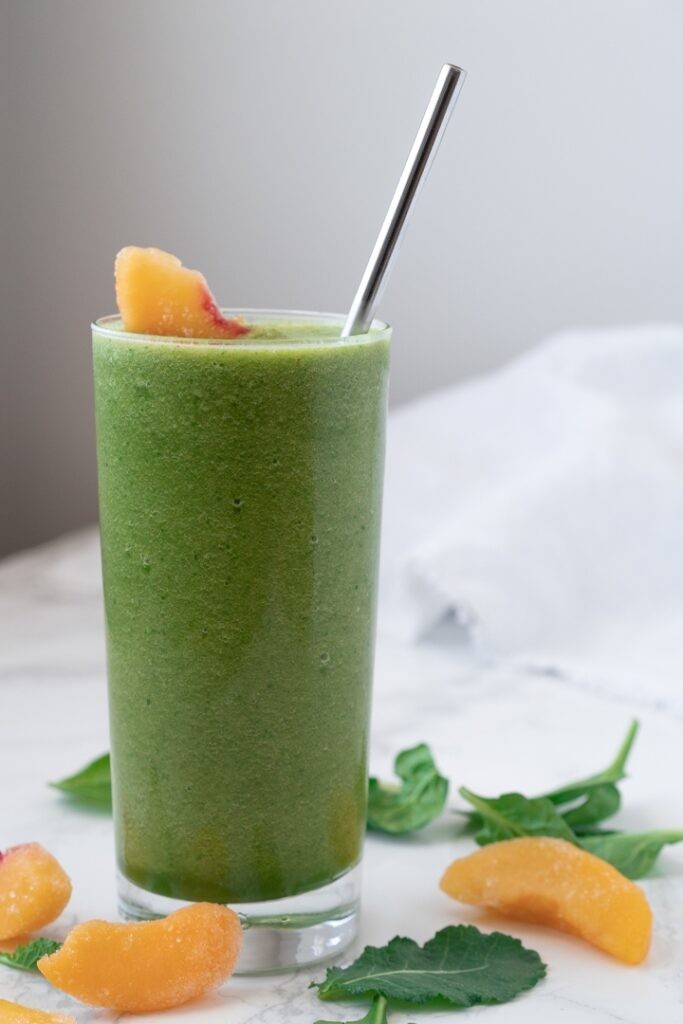 a vibrant green smoothie with visible pieces of peach and parsley, garnished with a peach slice