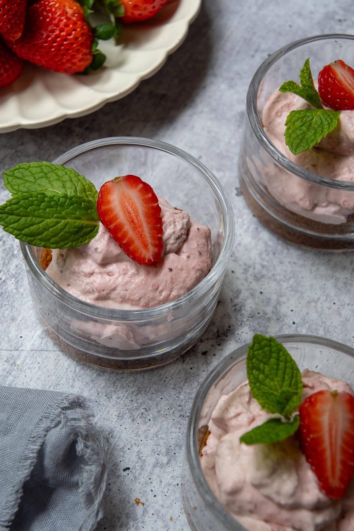 overhead shot of a light and airy strawberry cloud mousse in a glass cup, topped with fresh strawberries and a sprig of mint