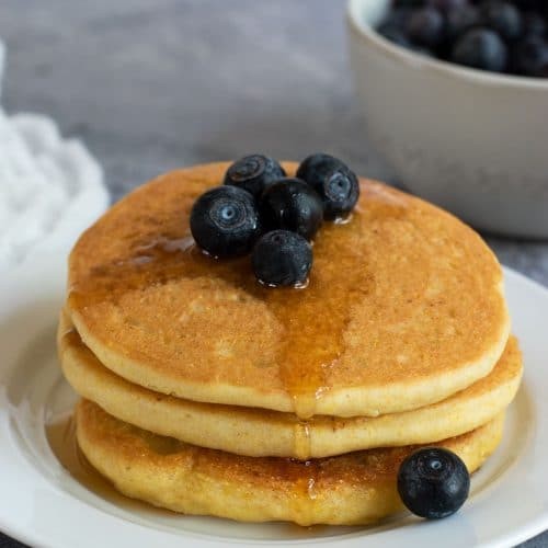 stack of gluten-free cornmeal pancakes with berries and syrup