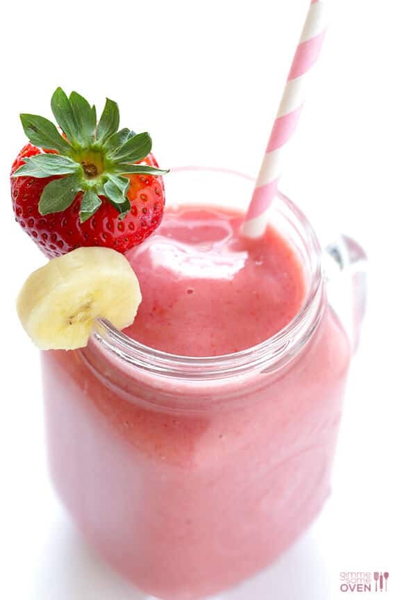 a glass of golden strawberry banana smoothie with fresh strawberries and bananas