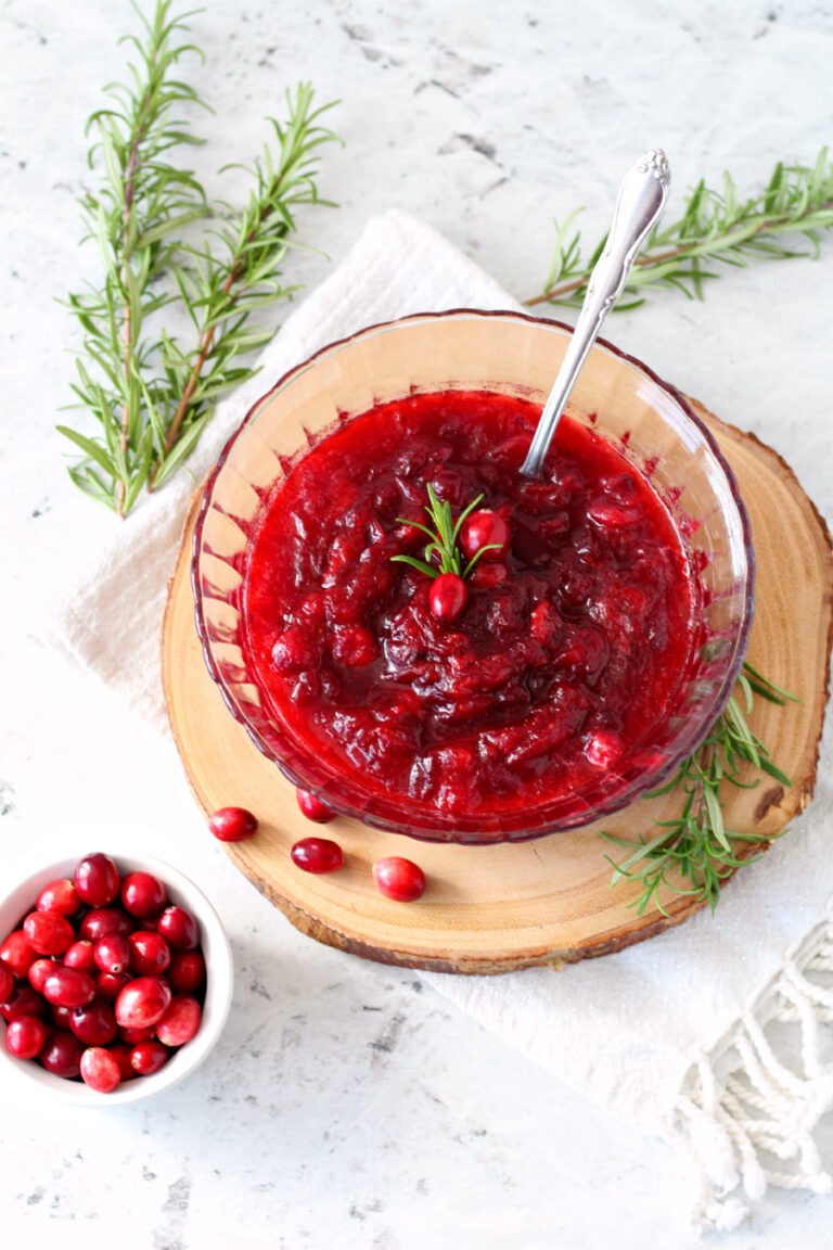 homemade cranberry sauce in a decorative bowl with fresh cranberries and rosemary garnish