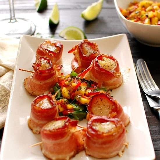 bacon wrapped scallops with mango salsa on a white plate