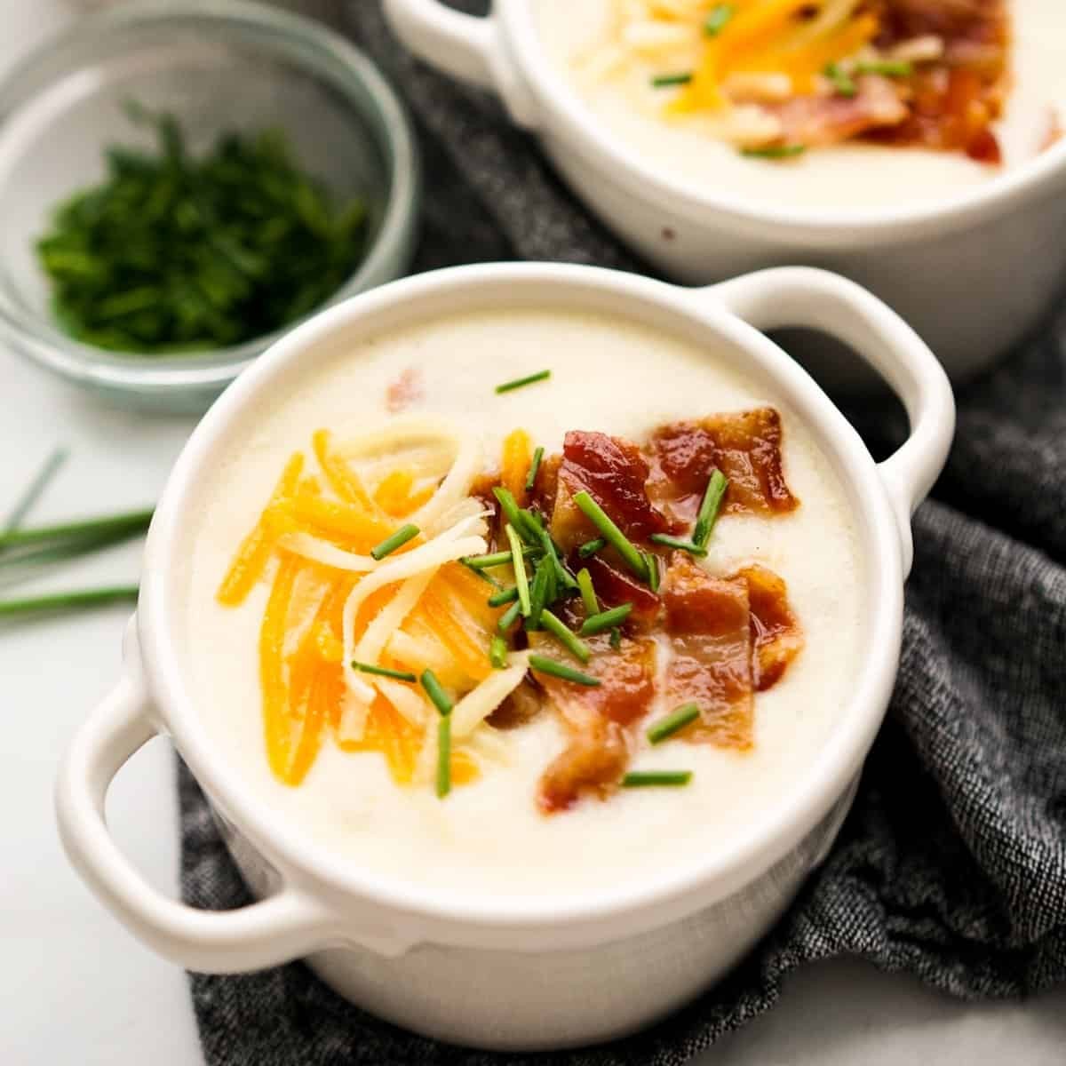 Hearty bowl of creamy cheddar potato soup garnished with chives and bacon bits, cozy setting