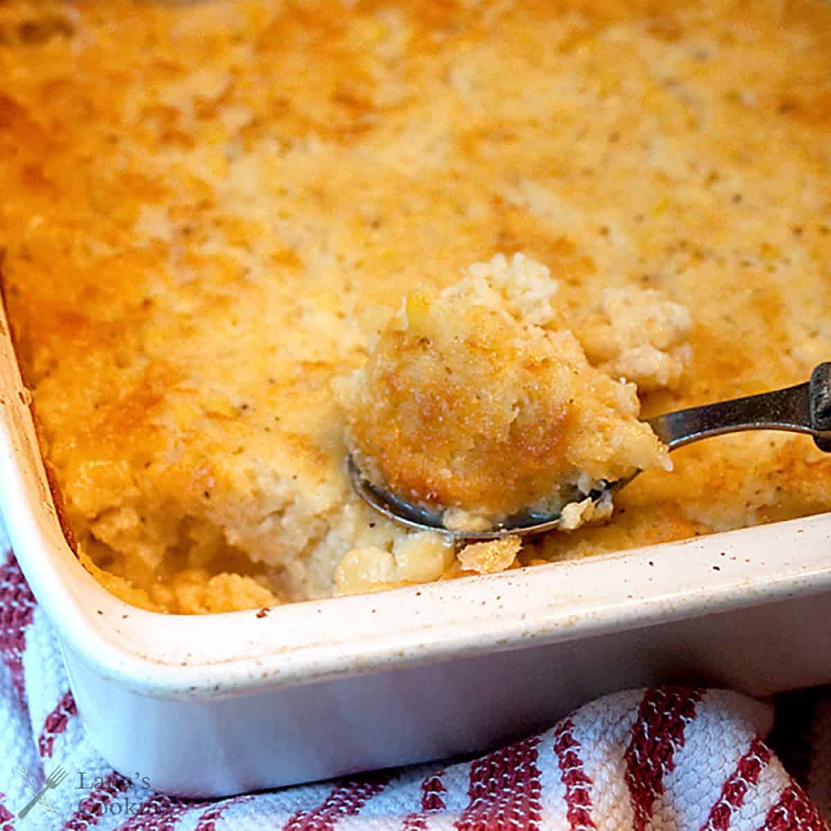Golden brown baked corn casserole with a spoon scooping out a portion, cozy kitchen setting
