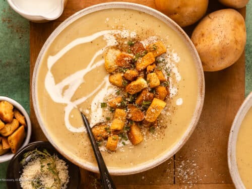 Steaming bowl of creamy roasted garlic potato soup with fresh chives, a slice of crusty bread on the side, cozy lighting, rustic setting