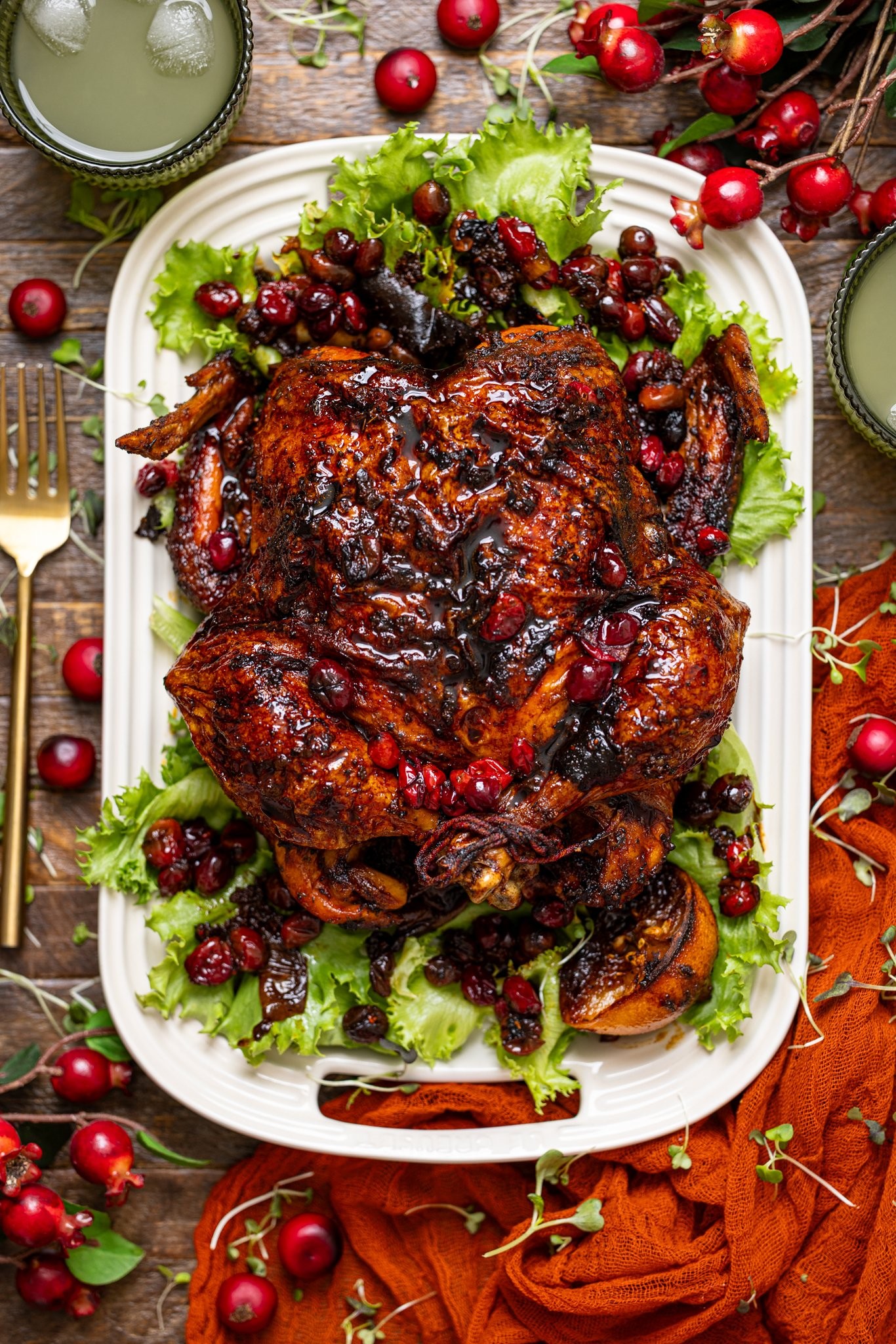 Roasted whole chicken with cranberry glaze, garnished with fresh herbs and cranberries on a festive Thanksgiving table