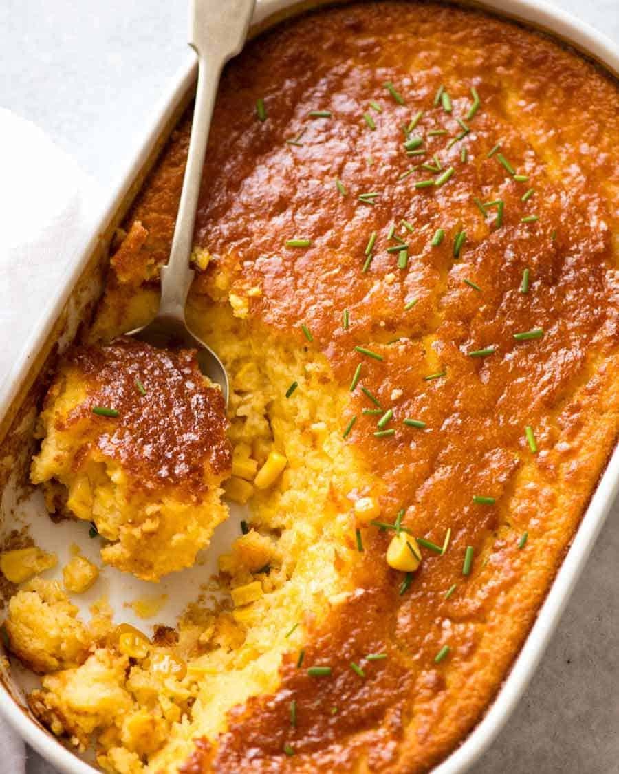 Warm baked corn casserole with golden-brown topping, fresh herbs