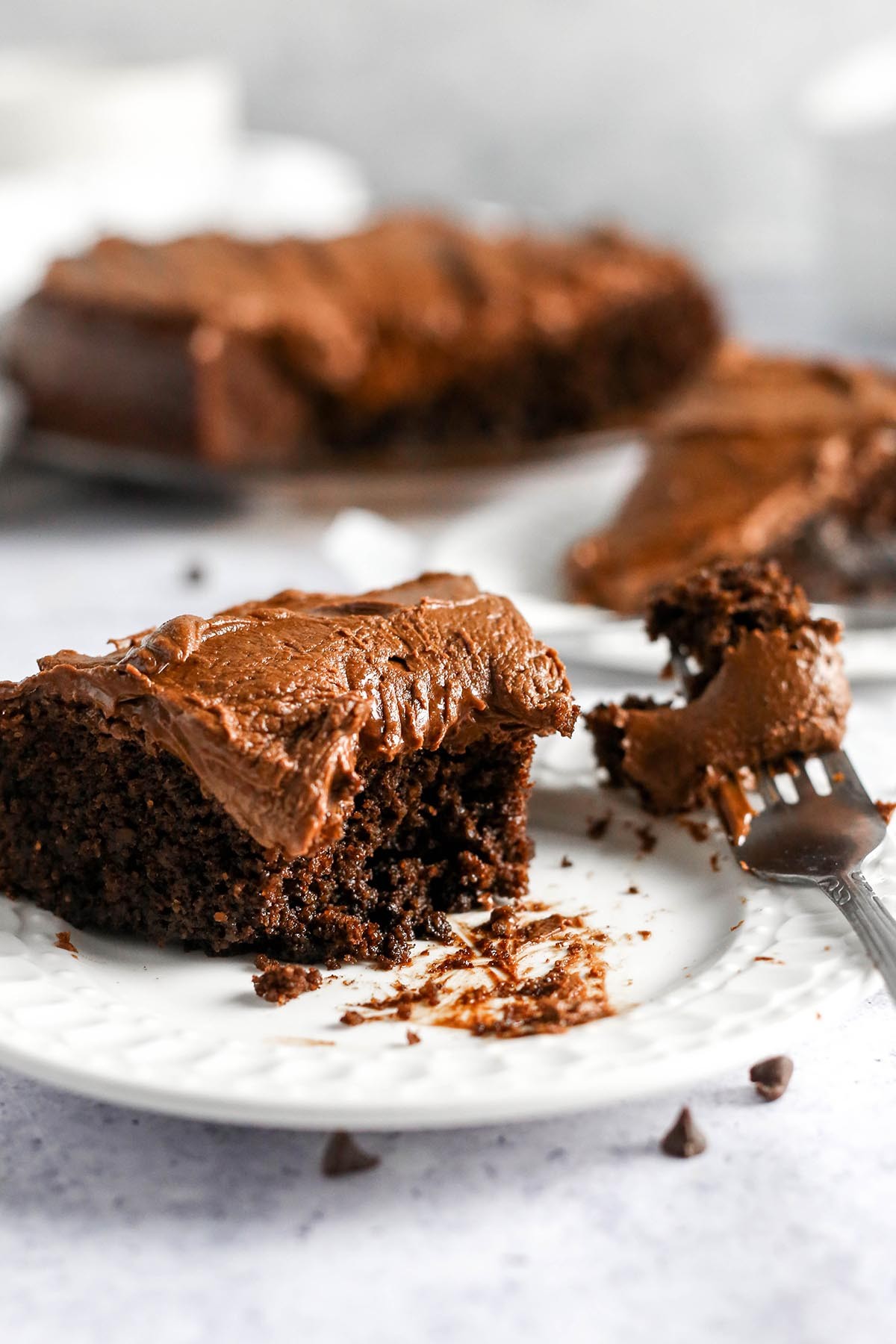 A close-up slice of rich, dark almond flour chocolate cake with a visible moist crumb, dusted with cocoa powder, next to a cup of hot coffee.