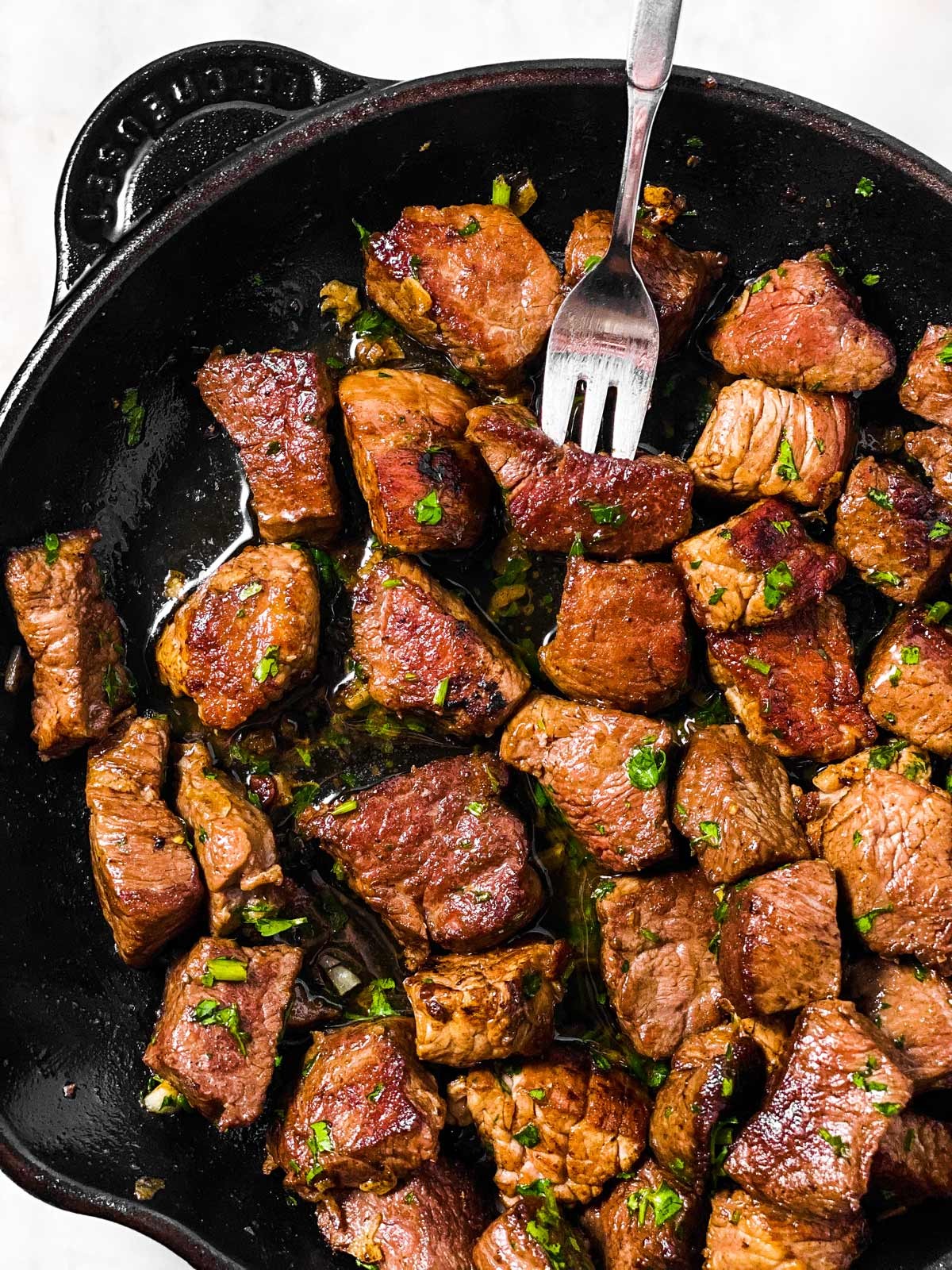 steak bites sizzling in garlic butter sauce in a cast iron pan