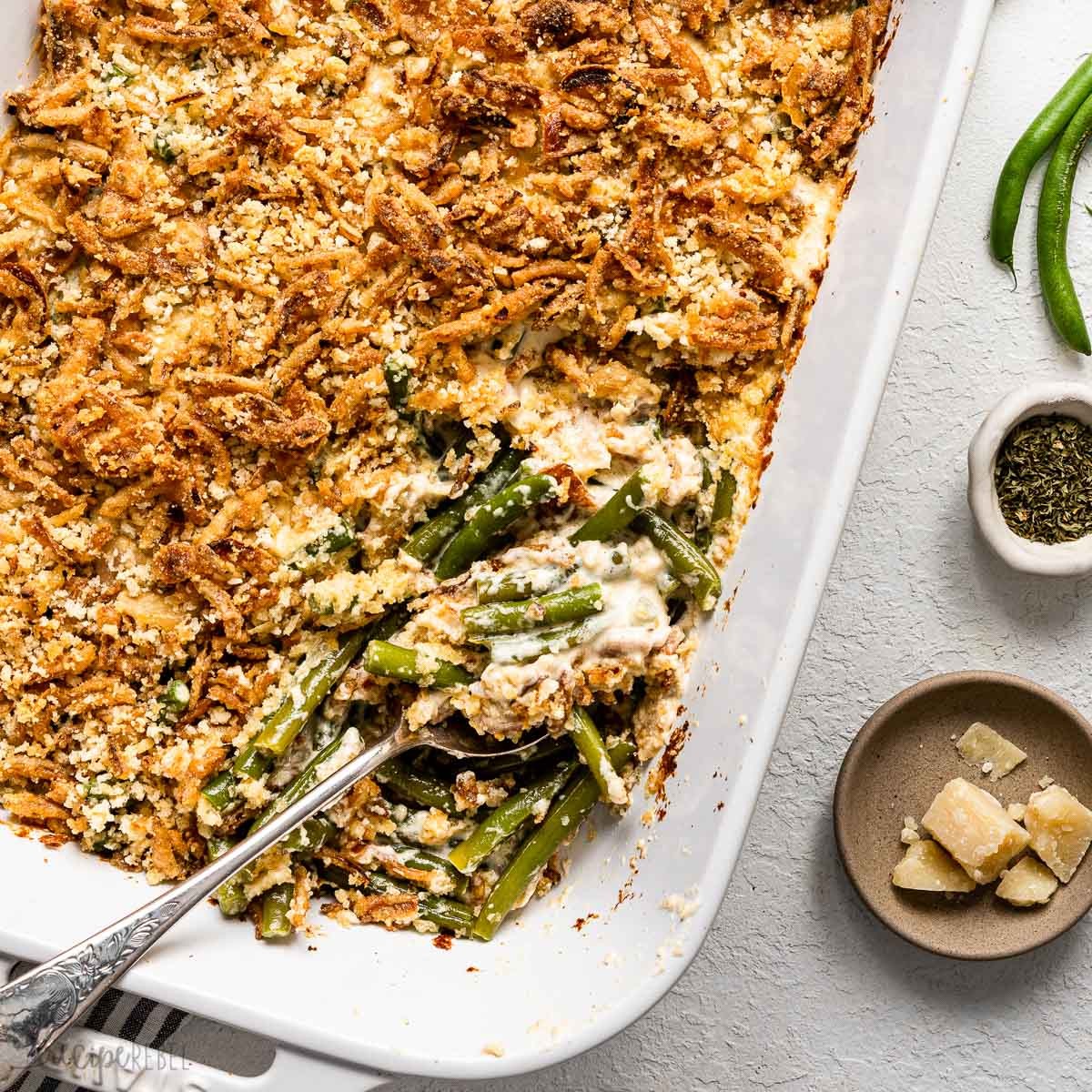 Close-up of a golden-brown Green Bean Parmesan Bake in a casserole dish, garnished with fresh parsley