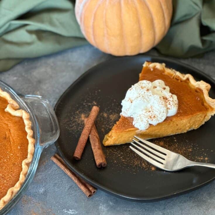 Rustic homemade creamy pumpkin pie with flaky butter crust, garnished with whipped cream and cinnamon, on a wooden table with fall decor