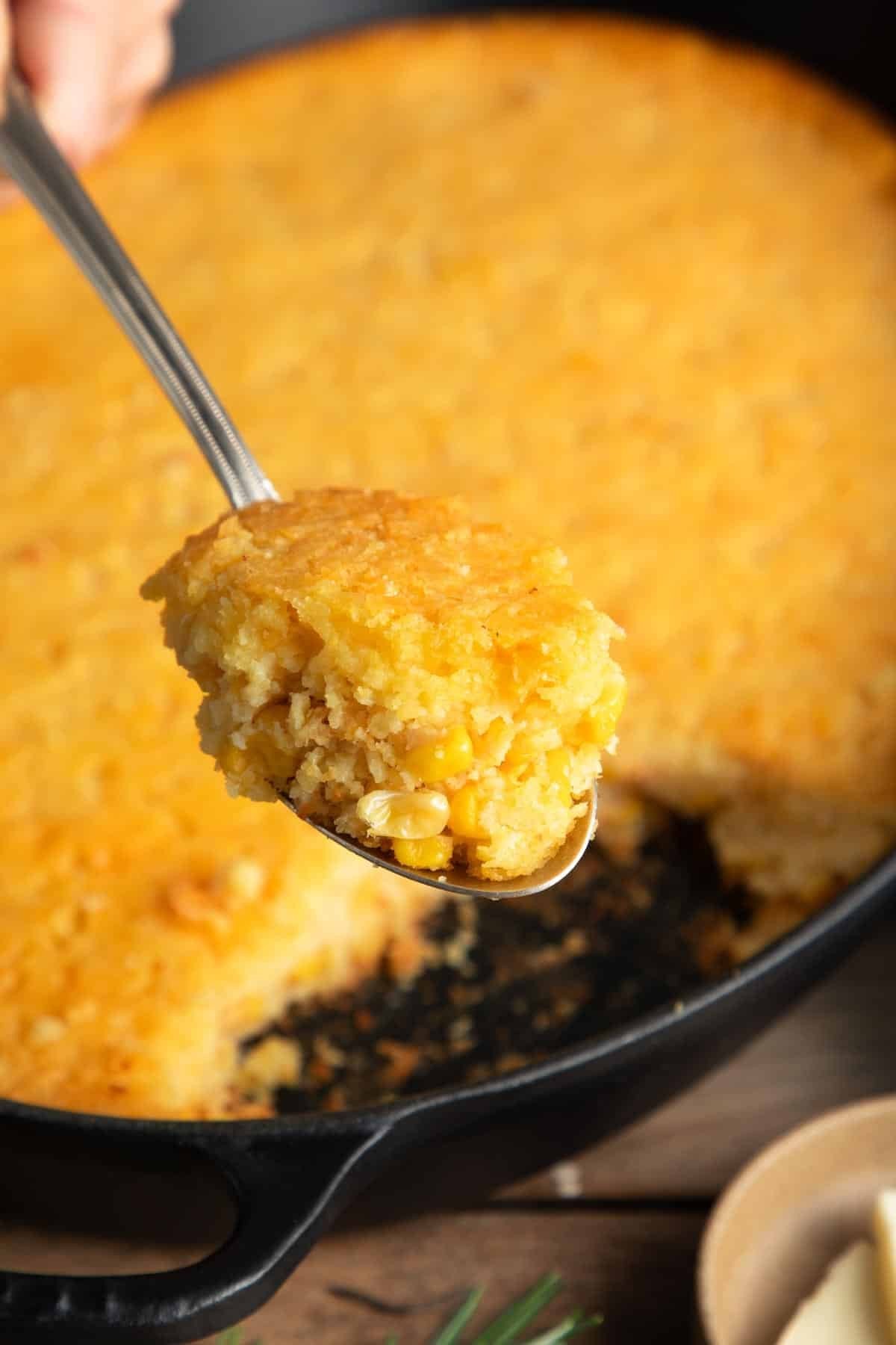 close up warm corn casserole with spoon, golden brown top, steaming
