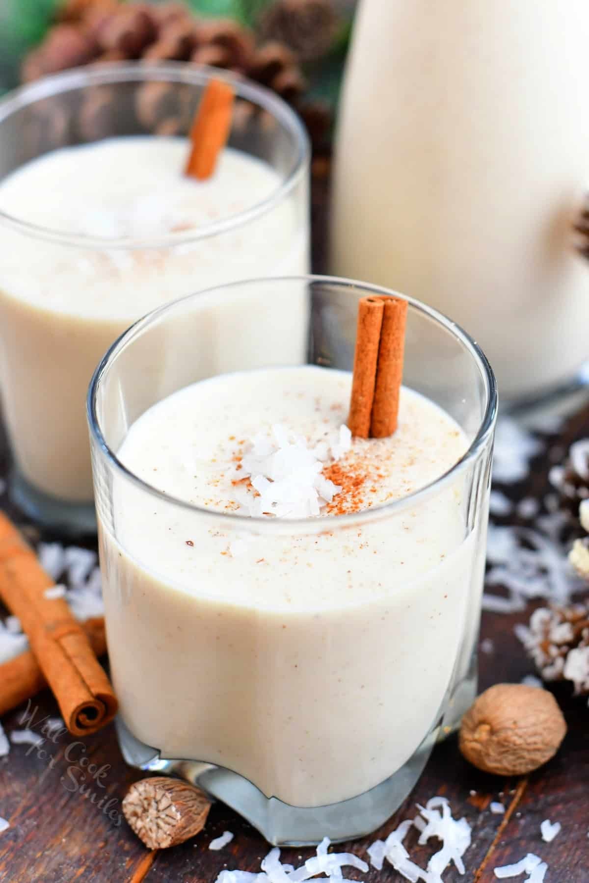 festive creamy coquito in a glass with toasted coconut flakes, cinnamon stick, and holiday decorations